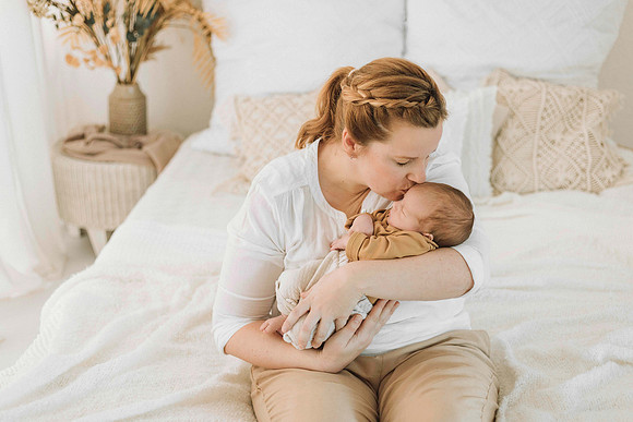 Babyfotografin Tettnang" – Mutter gibt ihrem Neugeborenen einen Kuss auf die Stirn während einem Fotoshooting im Studio, auf dem hellen Bett.