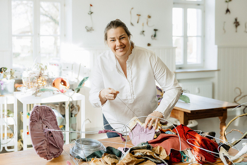 Atelierfotografie Allgäu-Bodensee: Künstlerin Anne Carnein lächelt beim Sortieren von Stoffen und Materialien für ihre Skulpturen.
