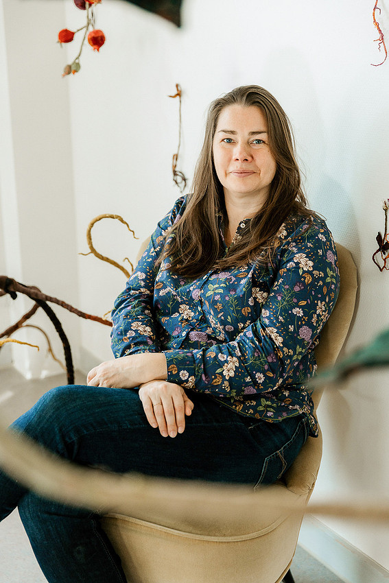 Businessfotografin für Künstler: Anne Carnein sitzt im modernen Portrait-Stil vor einer kunstvoll gestalteten Wand im Atelier.