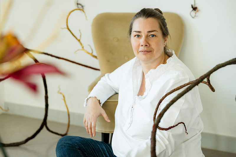 Professionelles Künstlerportrait: Anne Carnein in weißer Bluse sitzt entspannt auf einer Couch in ihrer Kreativwerkstatt am Bodensee.