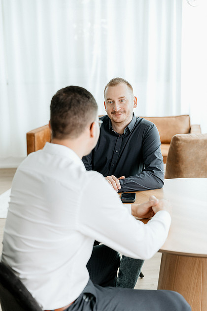 Unternehmensfotografie Ravensburg Geschäftsführer sitzt lächelnd am Besprechungstisch im Studio.