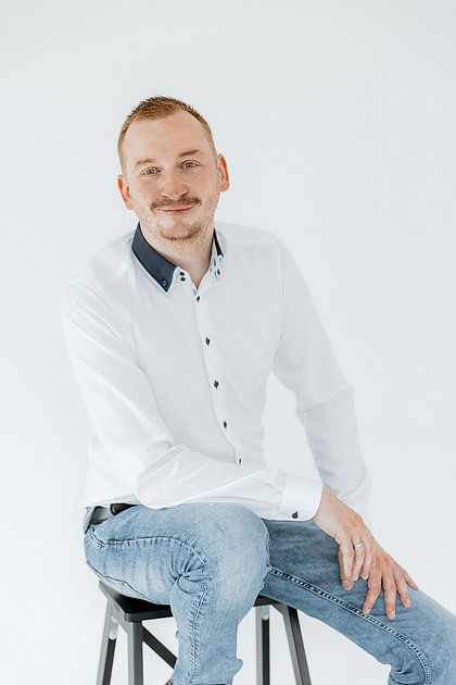 Portraitfotografie Weingarten Mann im weißen Hemd sitzt lächelnd auf einem Barhocker.